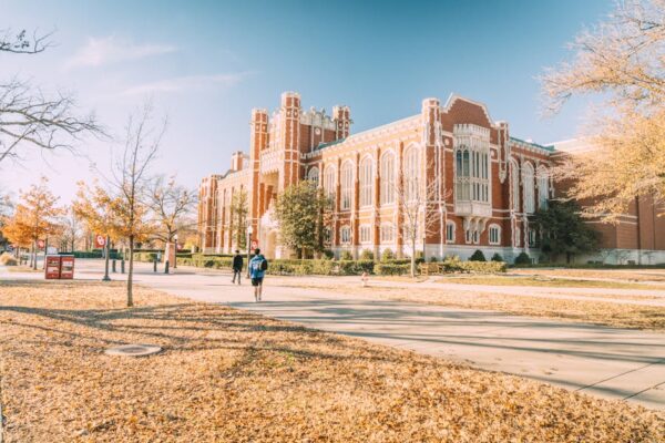 A university campus on an autumn afternoon, leaves on the ground and students walking to class