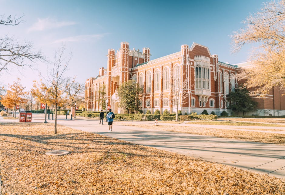 A university campus on an autumn afternoon, leaves on the ground and students walking to class