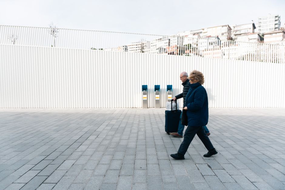 An older couple walking through an airport plaza with their luggage